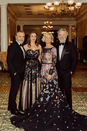 Four elegantly dressed guests pose together in a grand ballroom lobby at a formal gala.