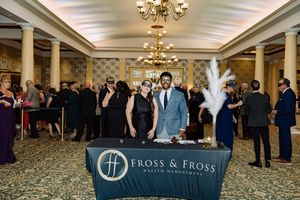 Two guests in masquerade masks pose at a Fross & Fross Wealth Management table at an elegant gala event.