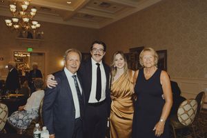 Two couples pose together for a photo in a grand ballroom at a formal gala event.