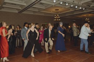 Formally dressed guests enjoy line dancing on the ballroom floor at an elegant gala event.