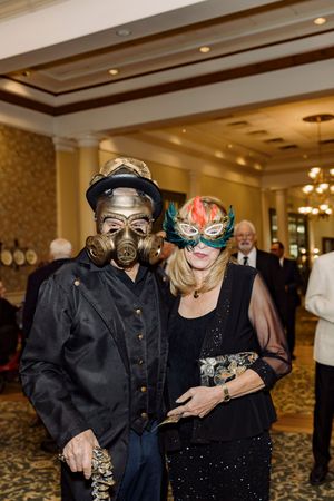 Two guests in elaborate masquerade masks pose together at a formal masquerade ball event.