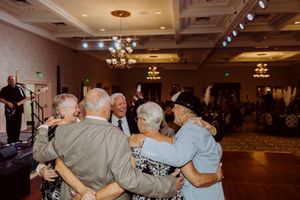Group of elderly guests share a warm embrace on a ballroom dance floor at a formal event.