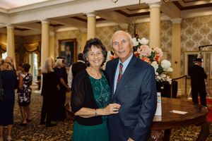 Smiling older couple posing together at formal event, woman in green dress, man in blue suit.