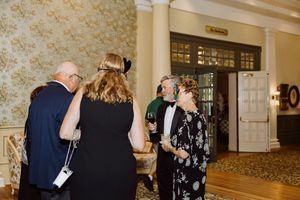 Guests mingle in formal attire at an elegant indoor gala event with classic wallpaper decor.