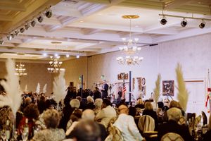 Large crowd of formally dressed guests attend an elegant gala ceremony in a grand ballroom.