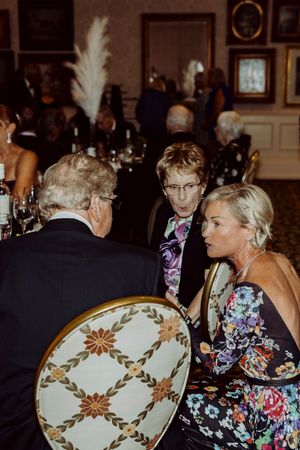 Guests in formal attire engage in conversation at a elegantly decorated banquet table.
