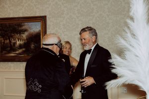Three formally dressed guests socializing at an upscale masquerade party event.