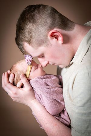 Father tenderly kissing his newborn baby girl wrapped in pink, holding her gently in his hands.