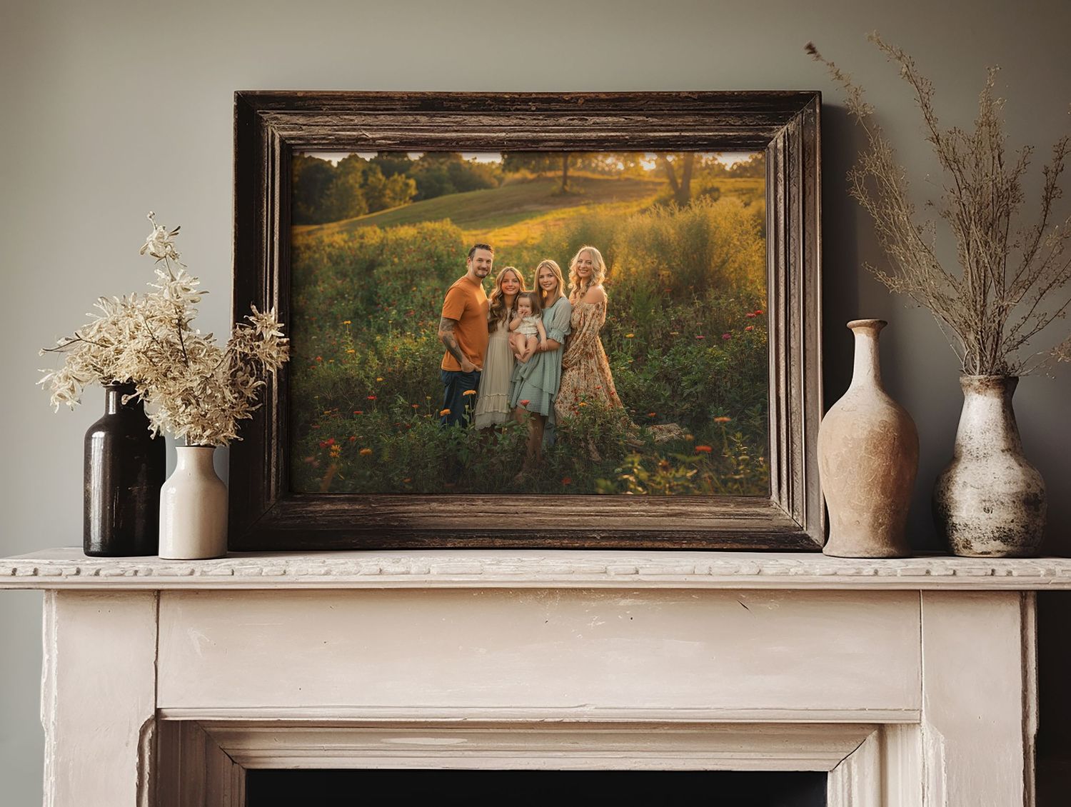 Framed family portrait photo displayed on a white fireplace mantel, surrounded by dried flower arrangements in vintage vases.