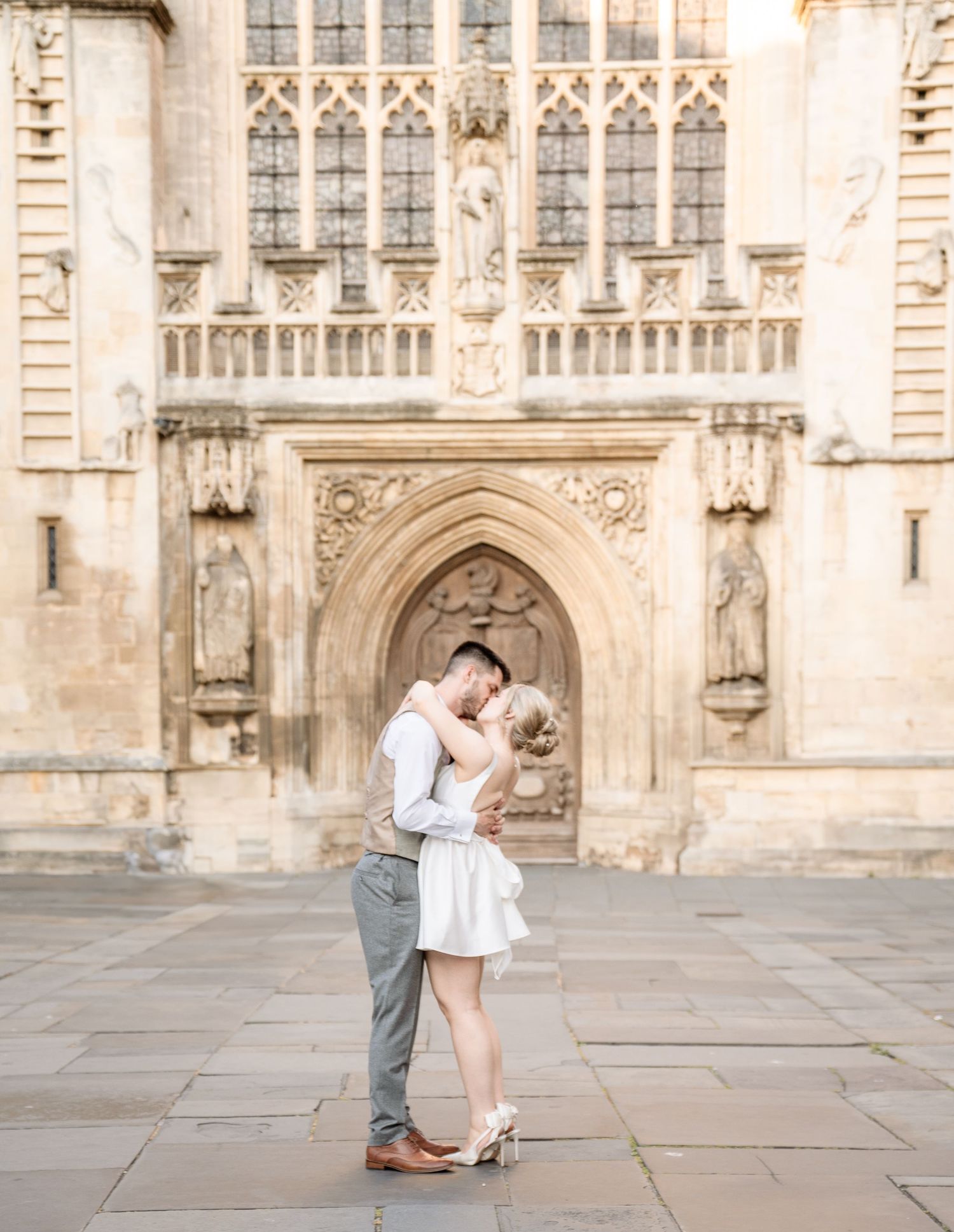 Couple sharing a romantic embrace in front of a stunning Gothic cathedral entrance in Bath, England.