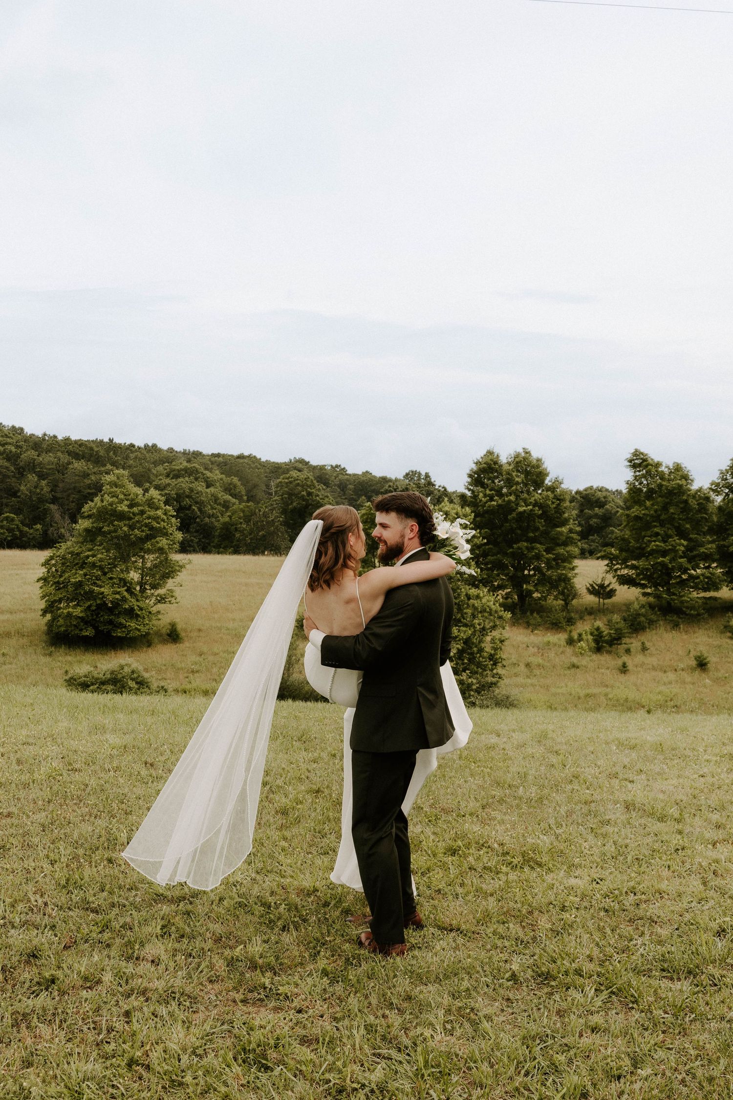 Bride and groom share a romantic dip kiss in a snowy winter landscape, surrounded by evergreen trees.