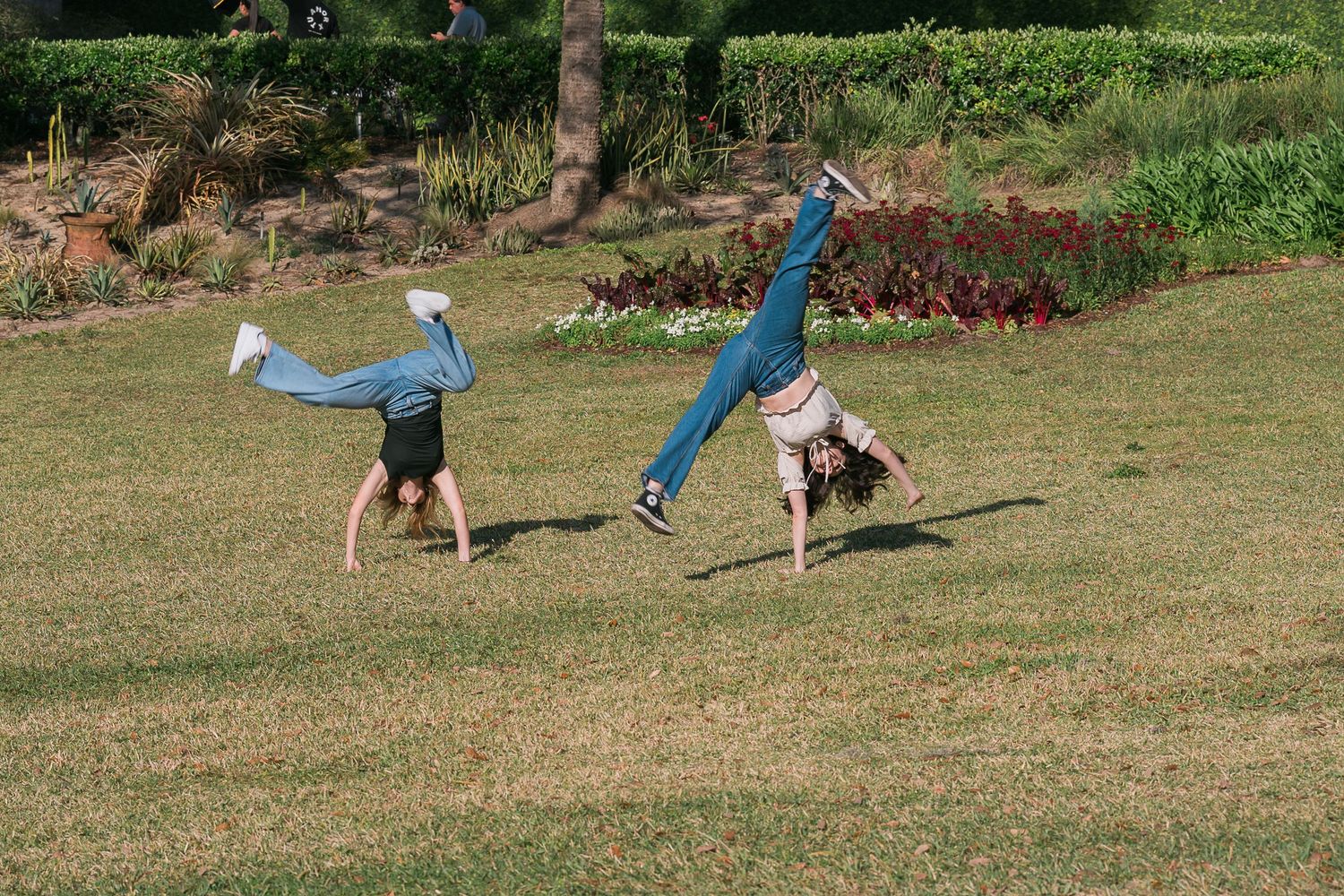 Children perform cartwheels and gymnastics moves on a grassy slope during a summer day.