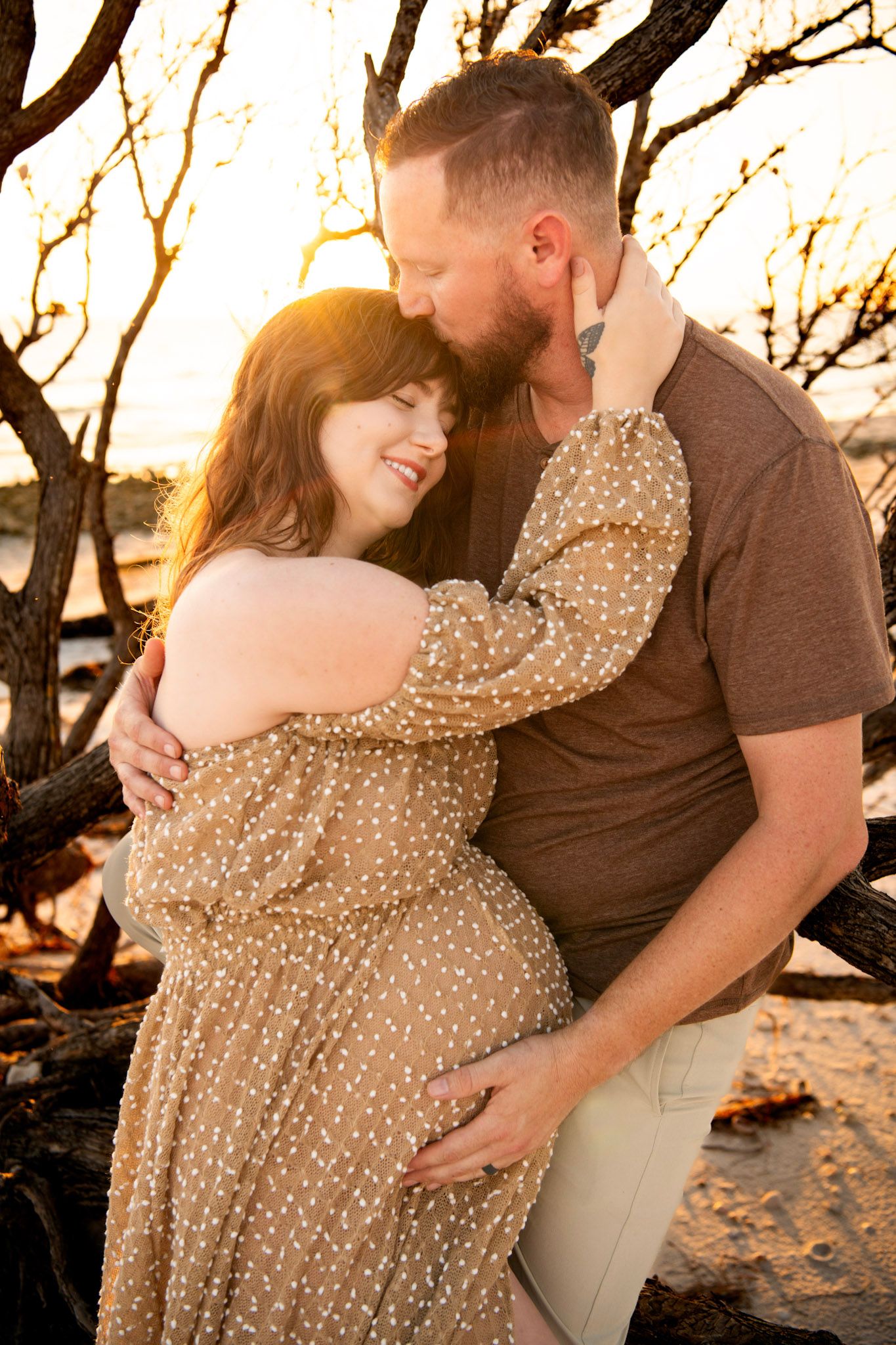 Intimate maternity photo of a couple embracing on a Dunedin, FL beach, capturing tender connection and warm evening coastal light.