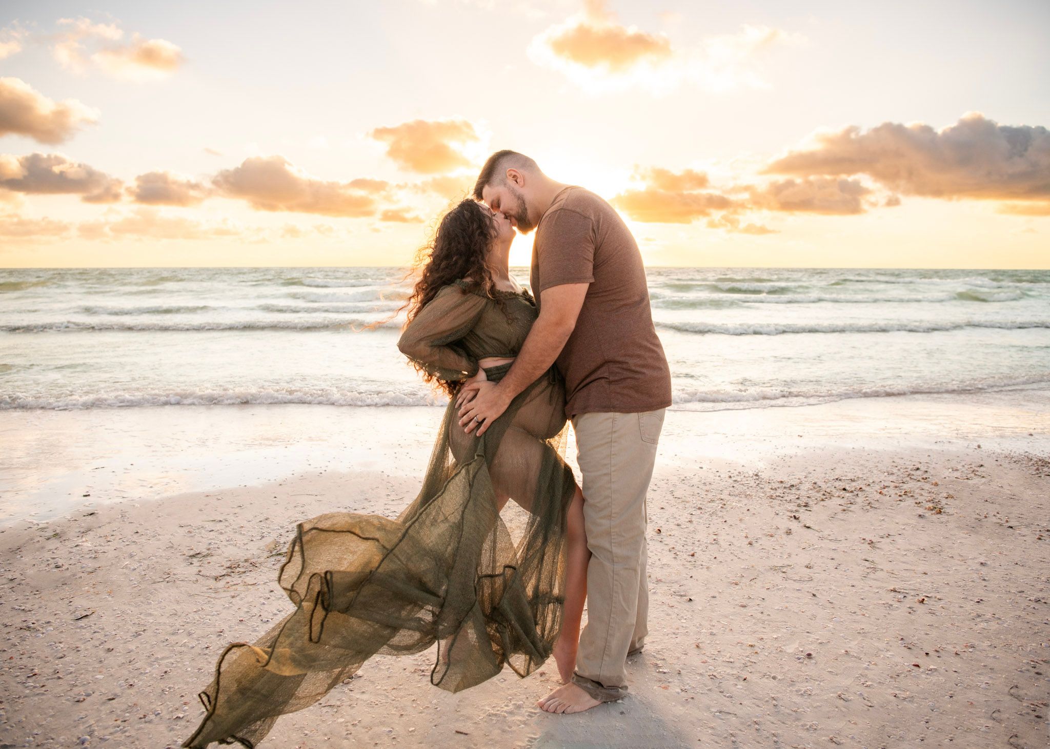 Expectant couple embraces at sunset on St. Pete Beach as a flowing emerald maternity gown catches the Gulf Coast breeze.