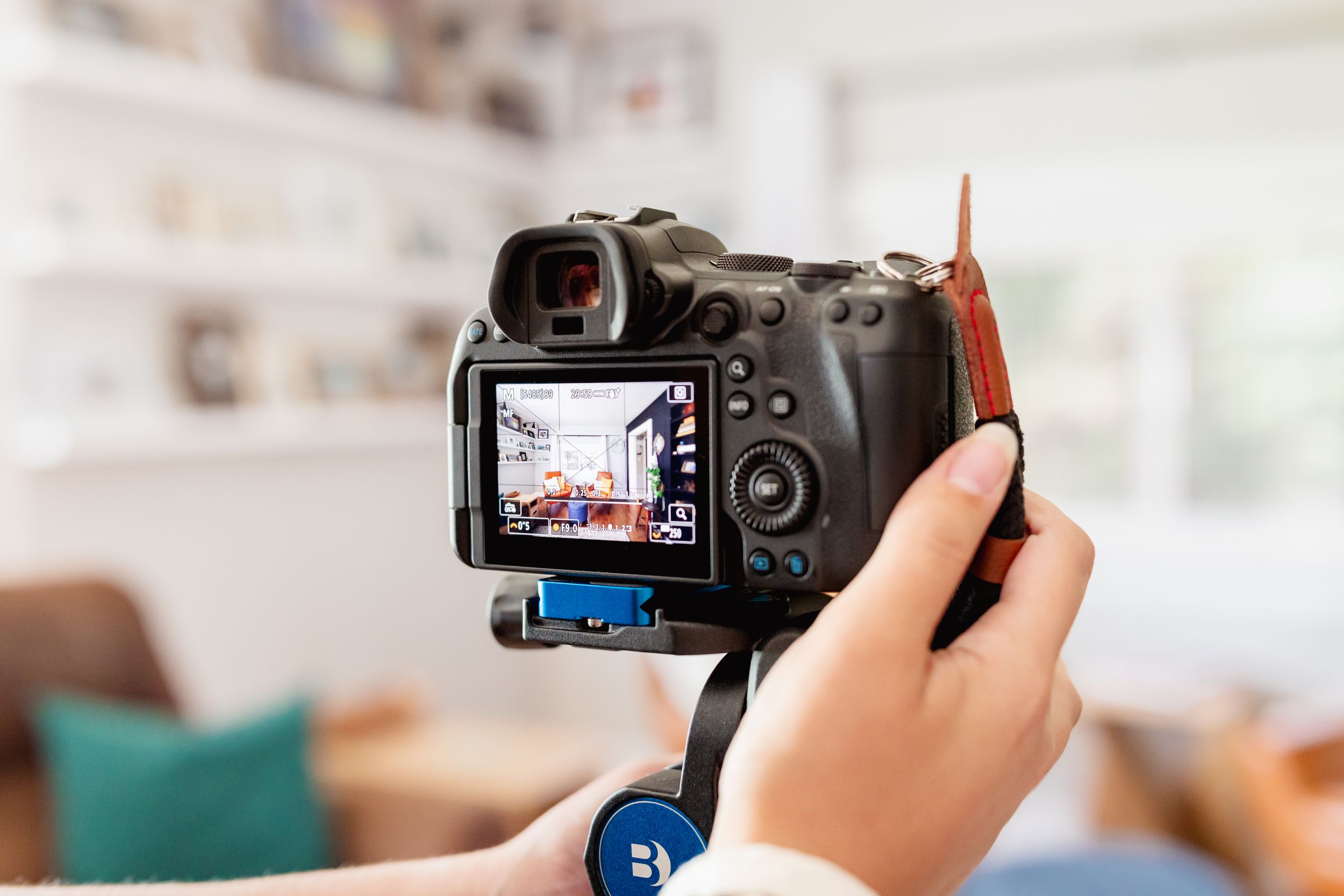 Person holding a DSLR camera on a mini tripod, capturing photos indoors with a bright living room in the background.