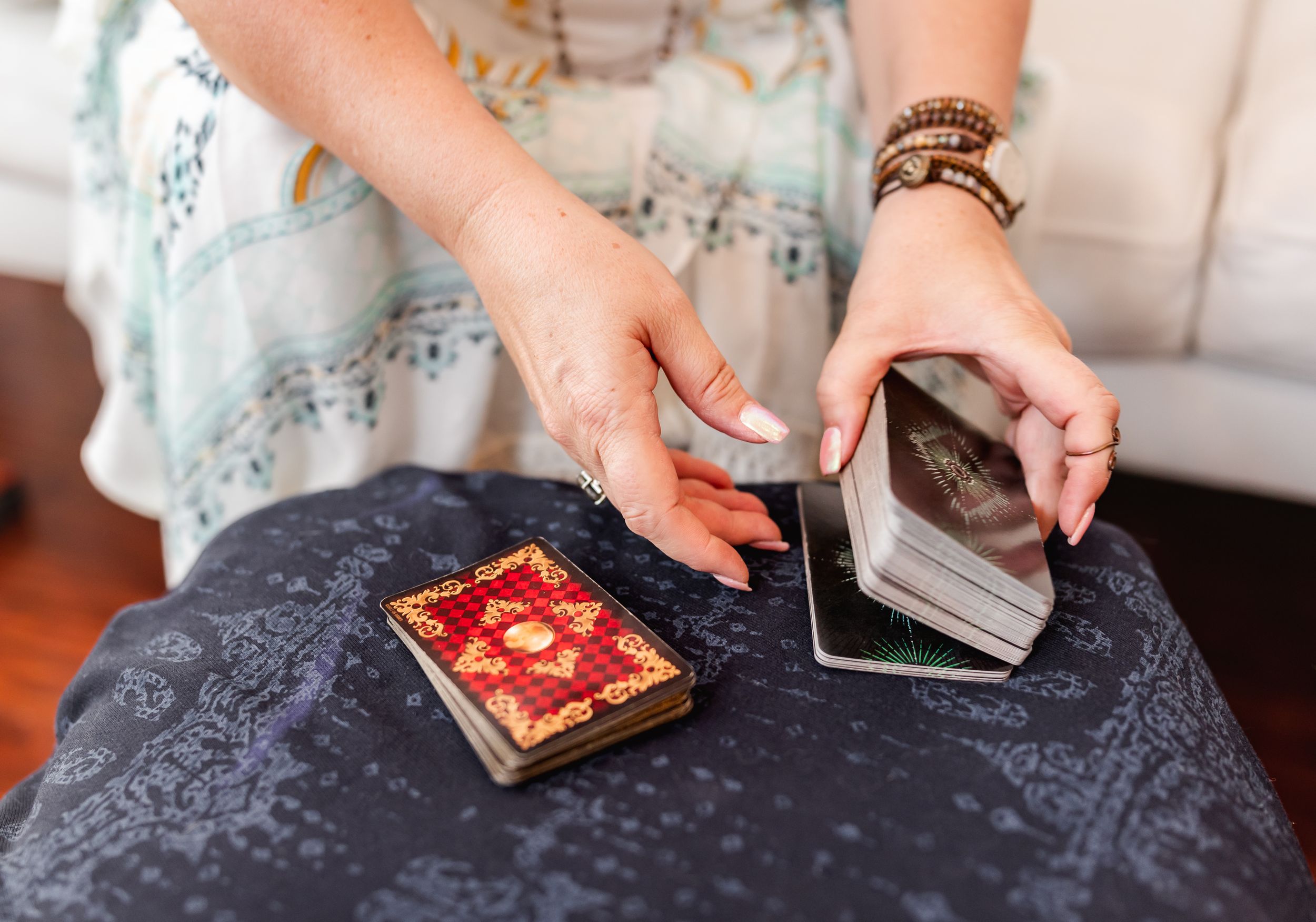 Hands shuffling tarot cards on dark cloth surface with ornate card deck nearby.