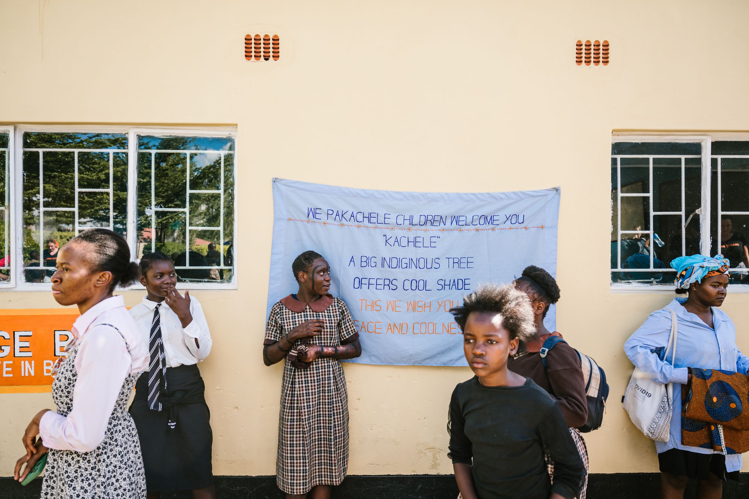 People queue outside a building under a banner in an African community gathering or voting event.