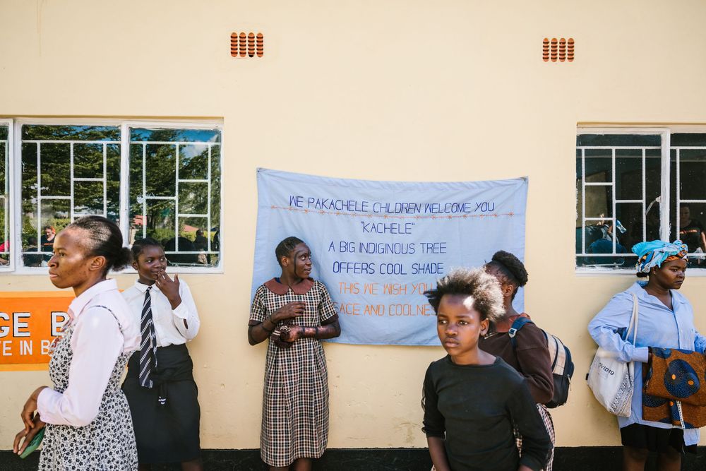 People queue outside a building under a banner in an African community gathering or voting event.