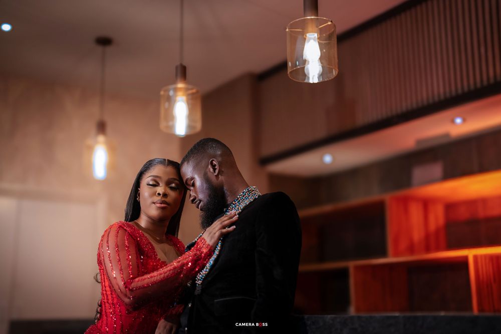 A couple shares an intimate moment under warm pendant lights in a stylish venue, woman in red lace dress.