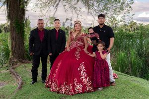 Family posing outdoors at a quinceañera celebration, featuring a girl in a red and gold ballgown with loved ones.