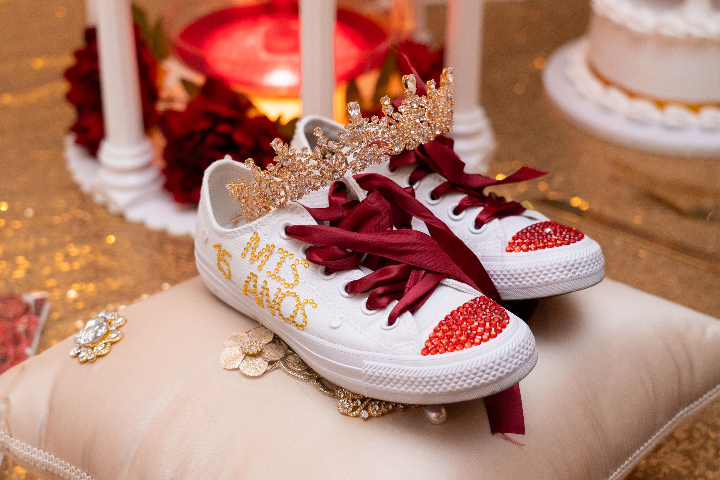 White Converse sneakers with red rhinestones, gold crown, and Miss 15 Anos text on a pillow for a quinceañera.