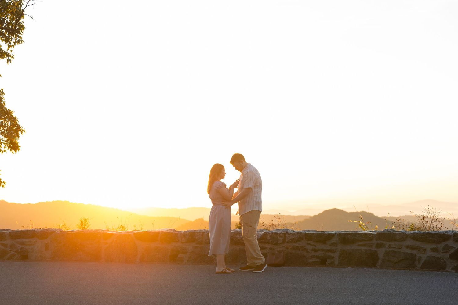 Couple holding hands silhouetted against a golden sunset with mountain views in the background.