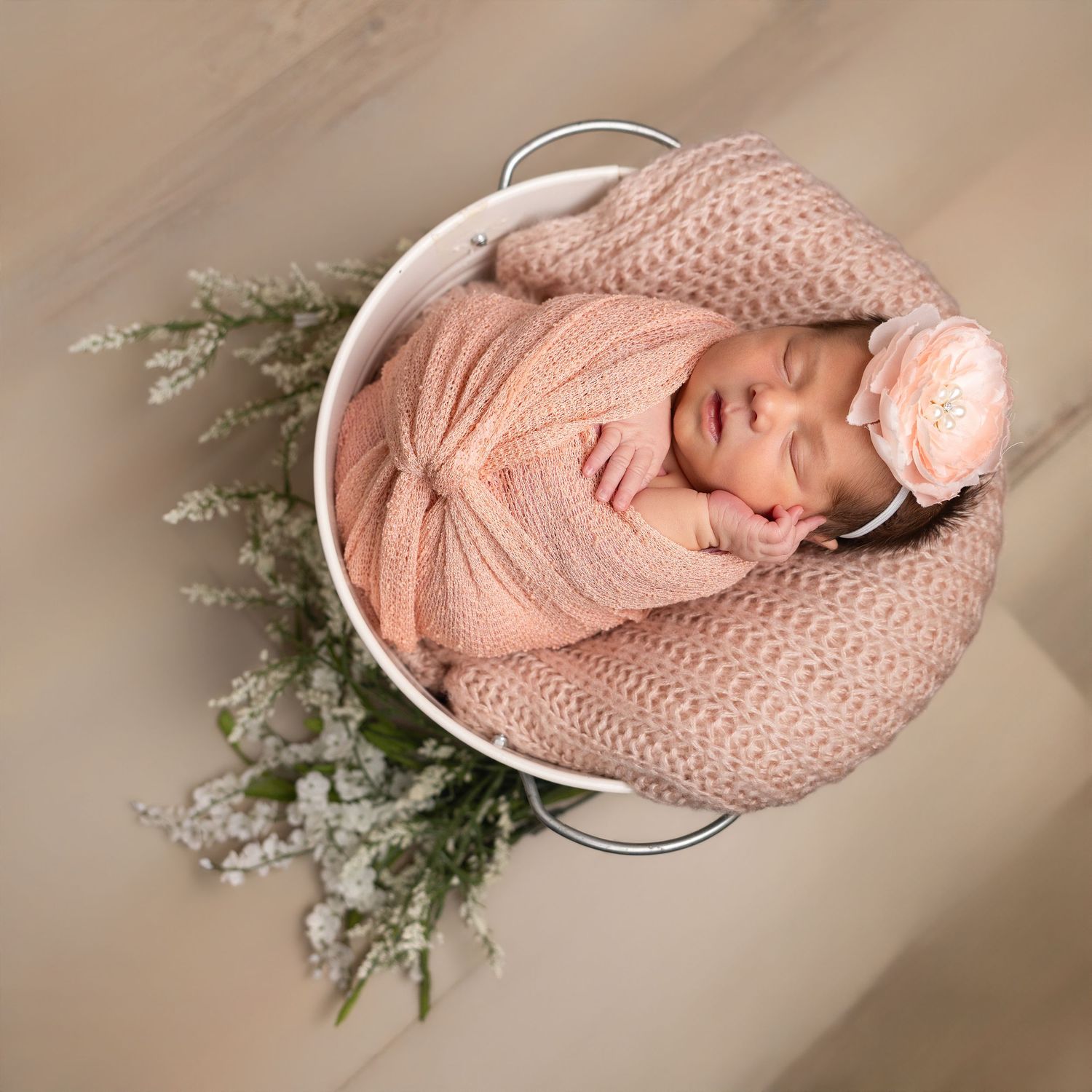 Sleeping newborn baby girl in lavender dress holding white bunny stuffed animal with purple flowers on pink background.