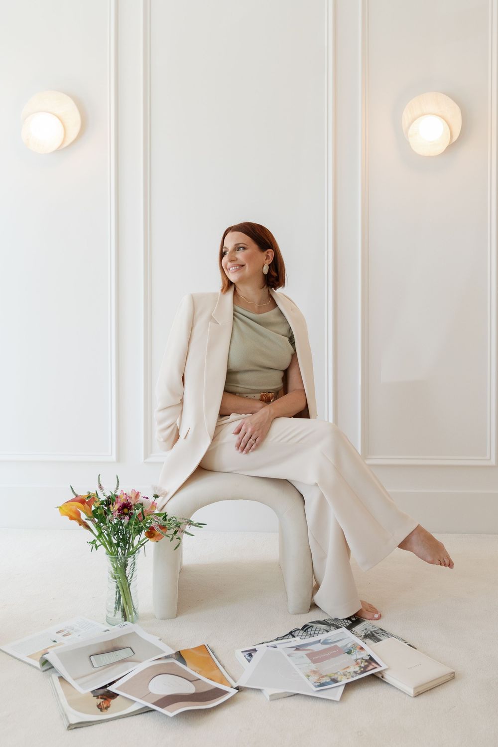 Smiling woman in a beige blazer seated in a bright white room.