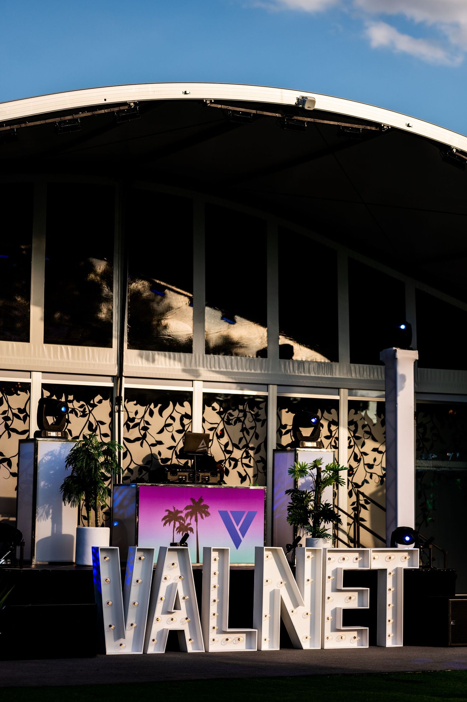 Large illuminated VALNET letters sign displayed outdoors at dusk with a DJ booth and colorful backdrop behind.