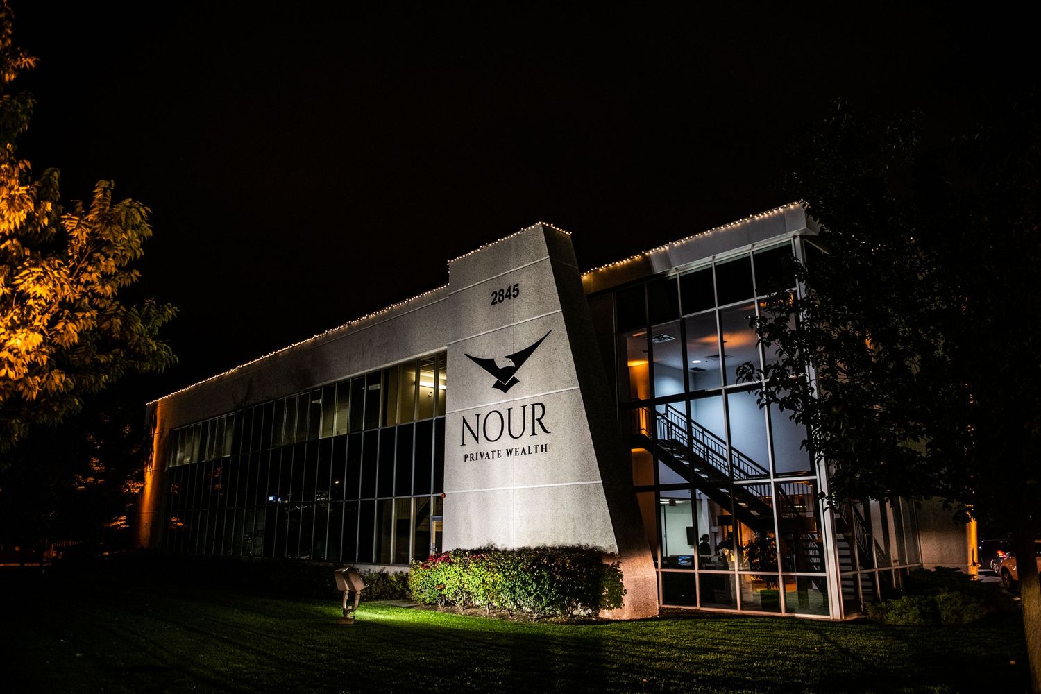 Nour Private Health clinic building exterior illuminated at night with modern glass facade and signage.