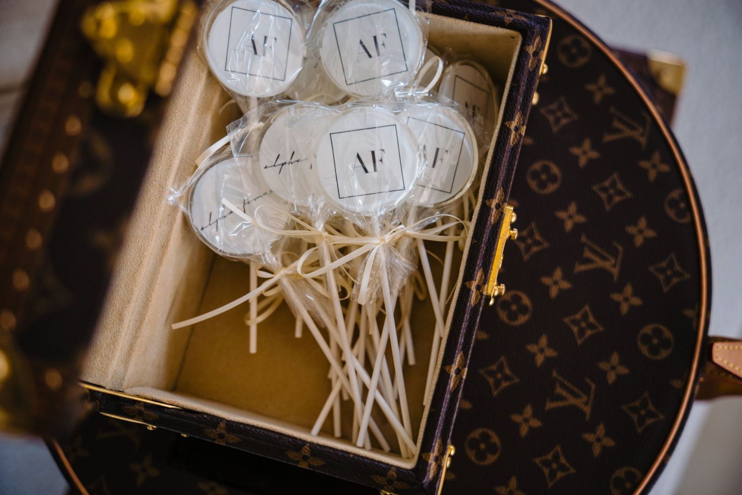 Custom monogram lollipops displayed in a Louis Vuitton hat box, perfect for luxury wedding favors.