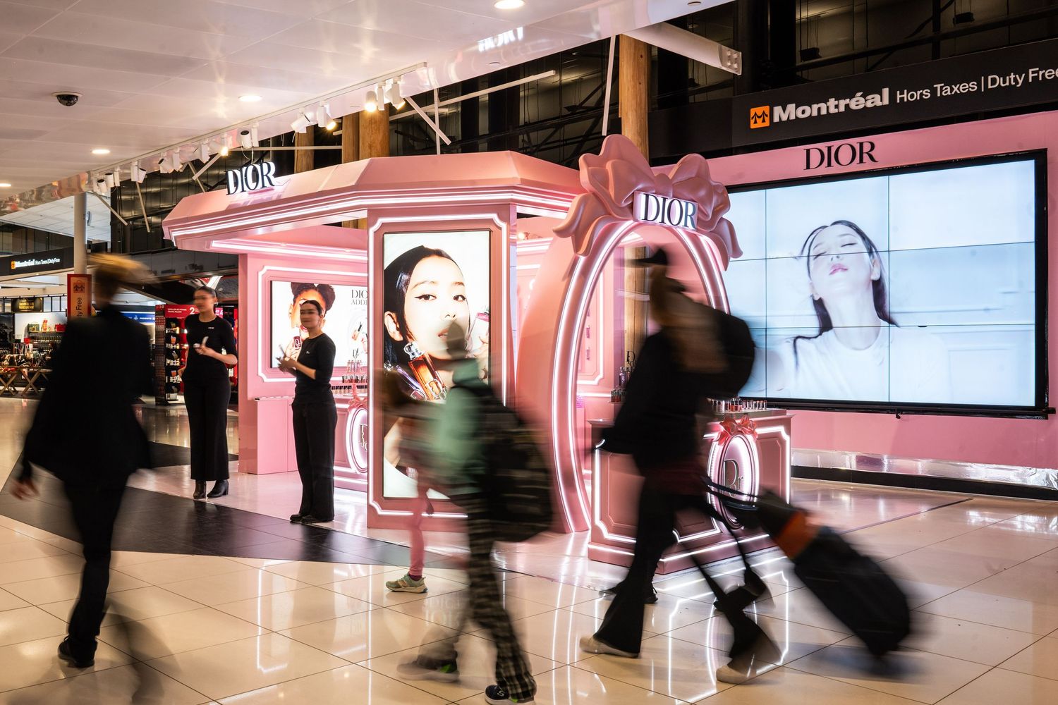 Dior duty-free pop-up shop at Montreal airport with pink display and shoppers walking past.