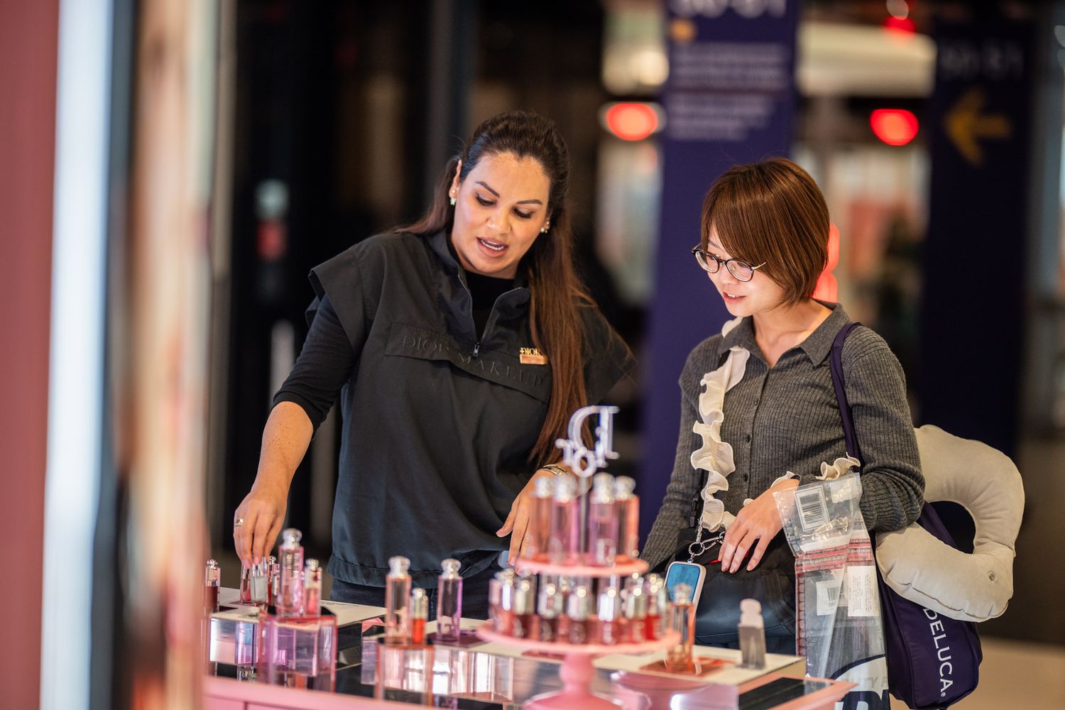 A beauty consultant assists a customer browsing cosmetics and perfumes at a retail display counter in a mall.