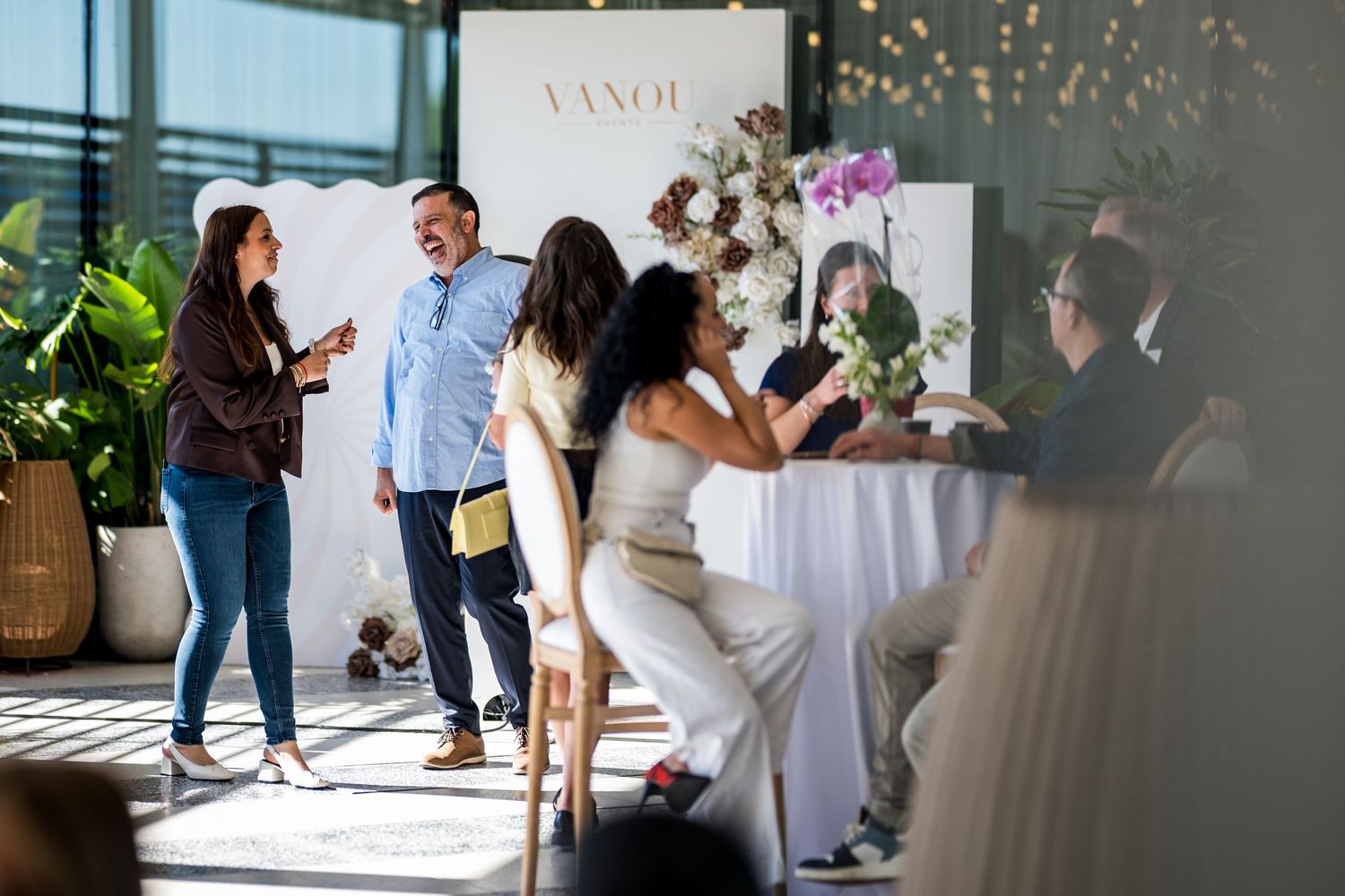 Guests mingle at a Vanola branded event in a modern venue with floral decor and natural light.