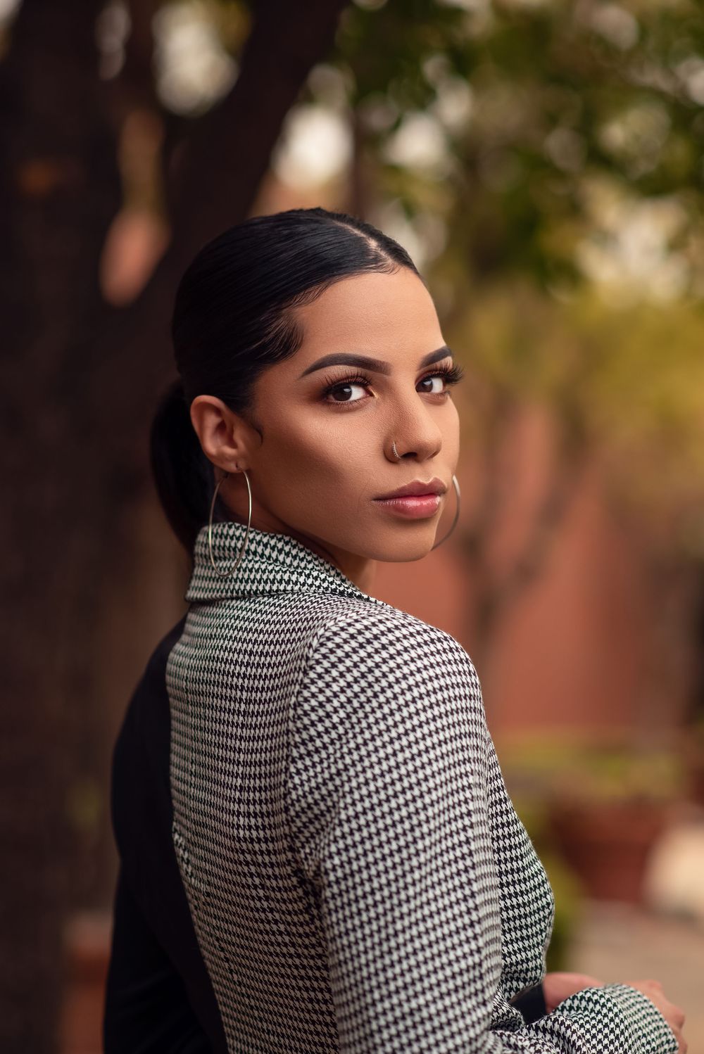 Outdoor beauty portrait of a woman with sleek dark hair looking over her shoulder in a patterned blazer.