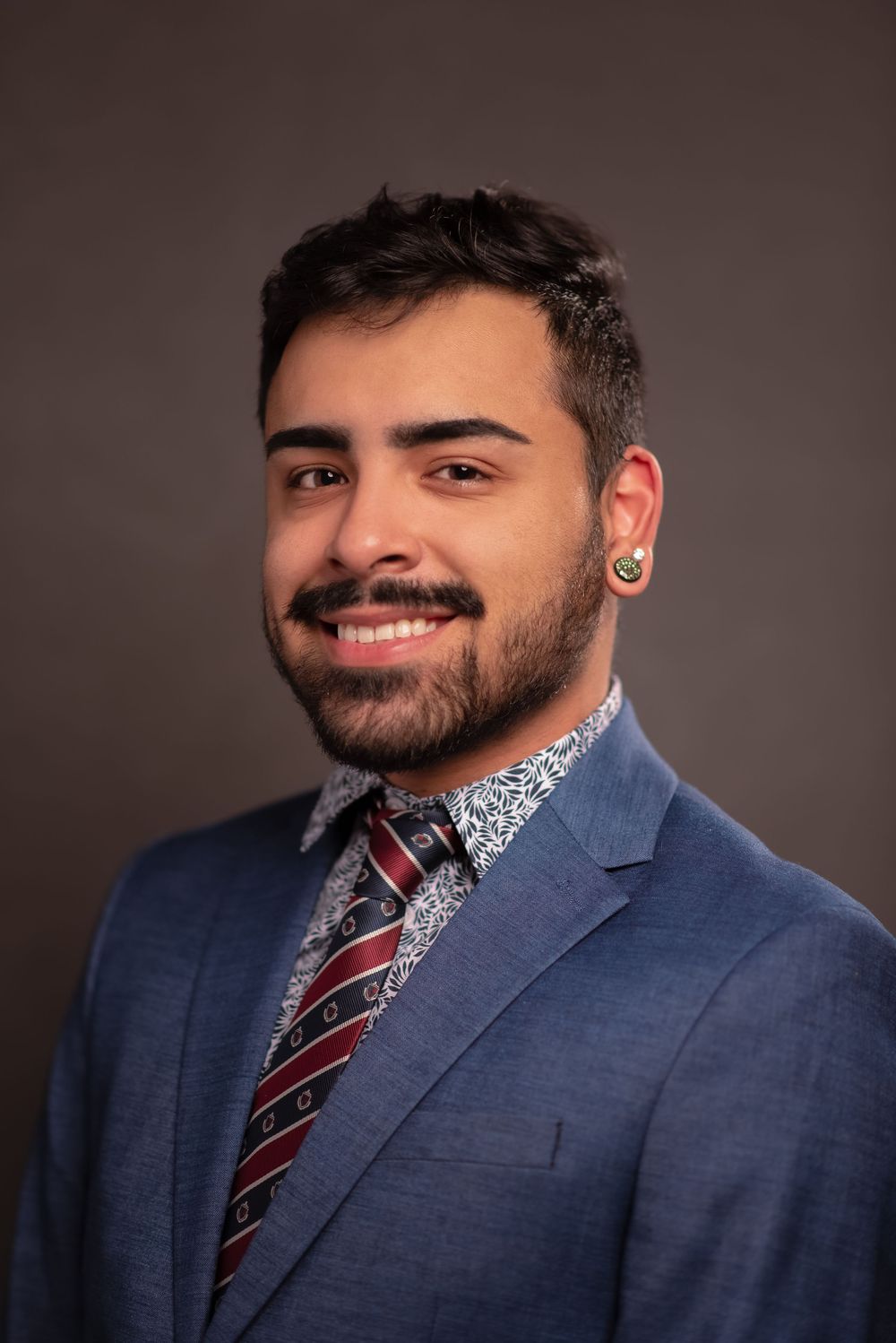 Professional studio headshot of a smiling man wearing a blue suit and striped tie.