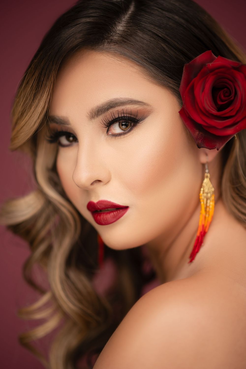 Glamour portrait of a woman with red lipstick, a red rose in her hair, and elegant dangling earrings.