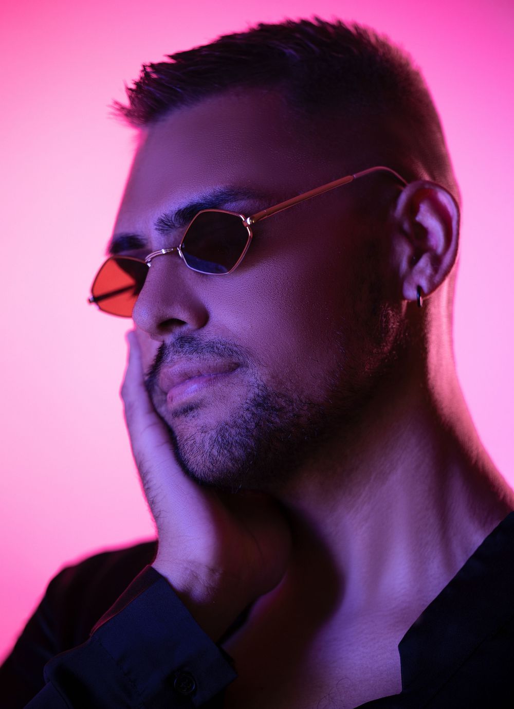 Creative neon-lit portrait of a man wearing tinted sunglasses under pink and purple lighting.