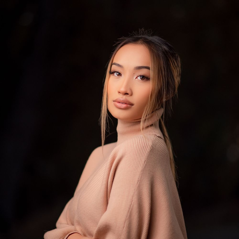 Elegant studio portrait of a woman in a beige sweater posing against a dark background.