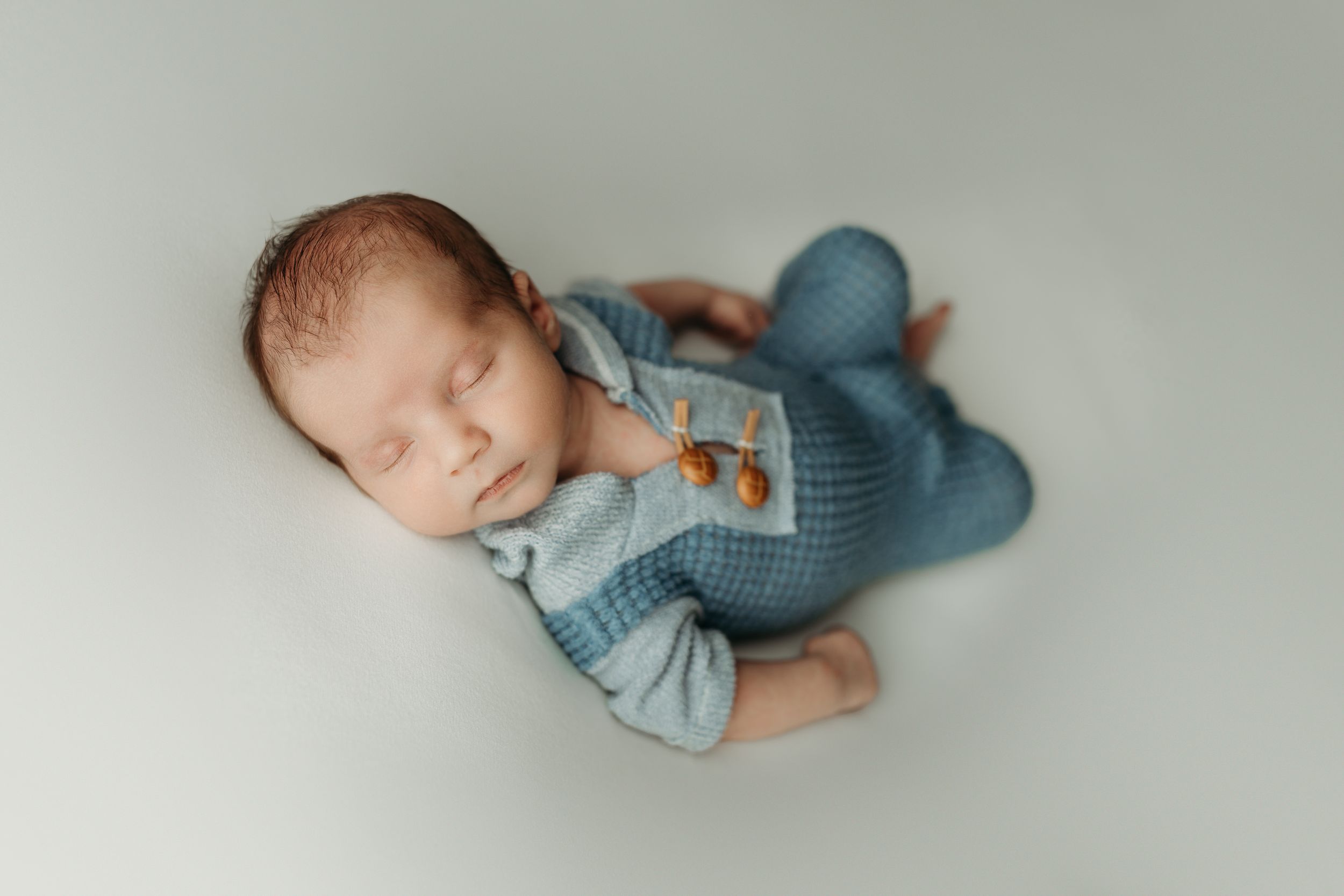 Sleeping newborn baby in blue knit romper lying peacefully on soft white background.