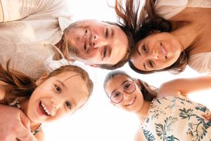 Four smiling family members huddle together in a circle, looking down at the camera with joy.