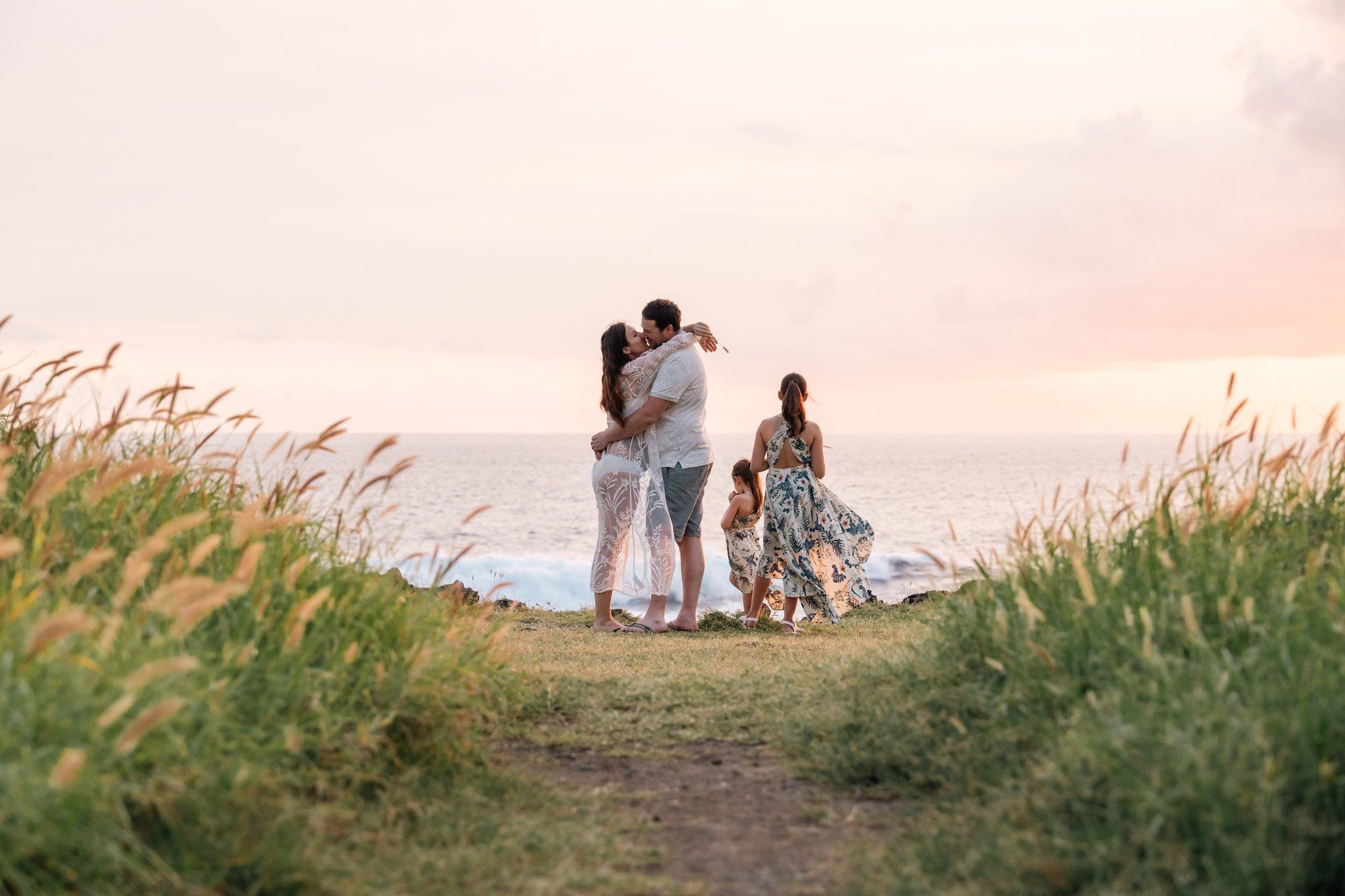 Family embracing at sunset on coastal cliffside with ocean view backdrop.