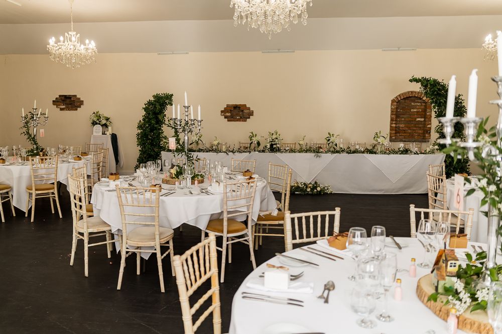 Elegant wedding reception hall with round tables, chiavari chairs, and floral centerpieces.