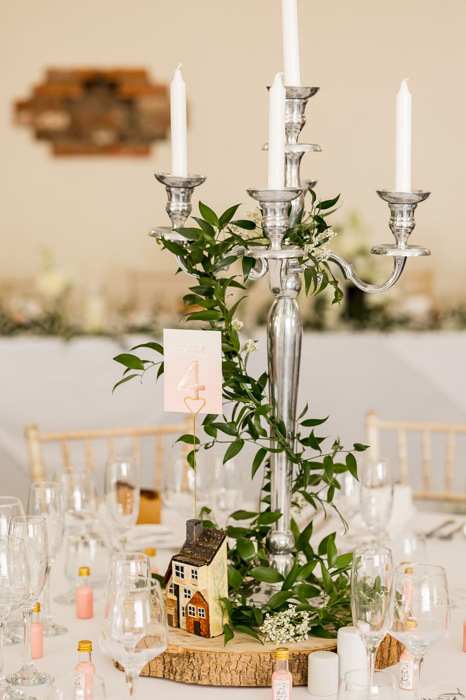 Silver candelabra centerpiece with greenery on wood slice at wedding reception table.