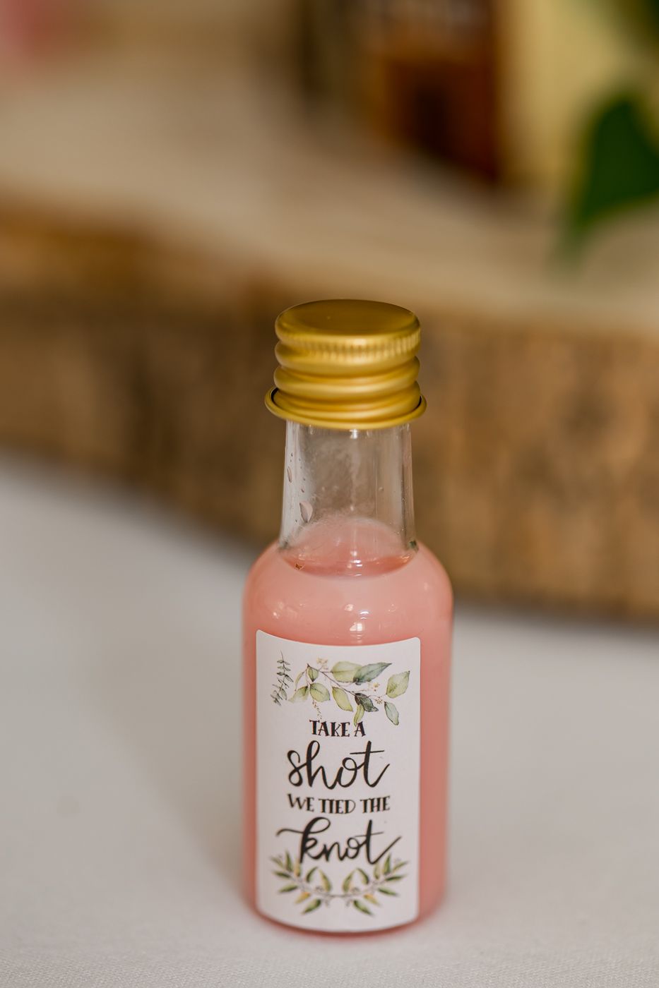 Mini pink liquor bottle wedding favor with gold cap and "Take a Shot We Tied the Knot" label.