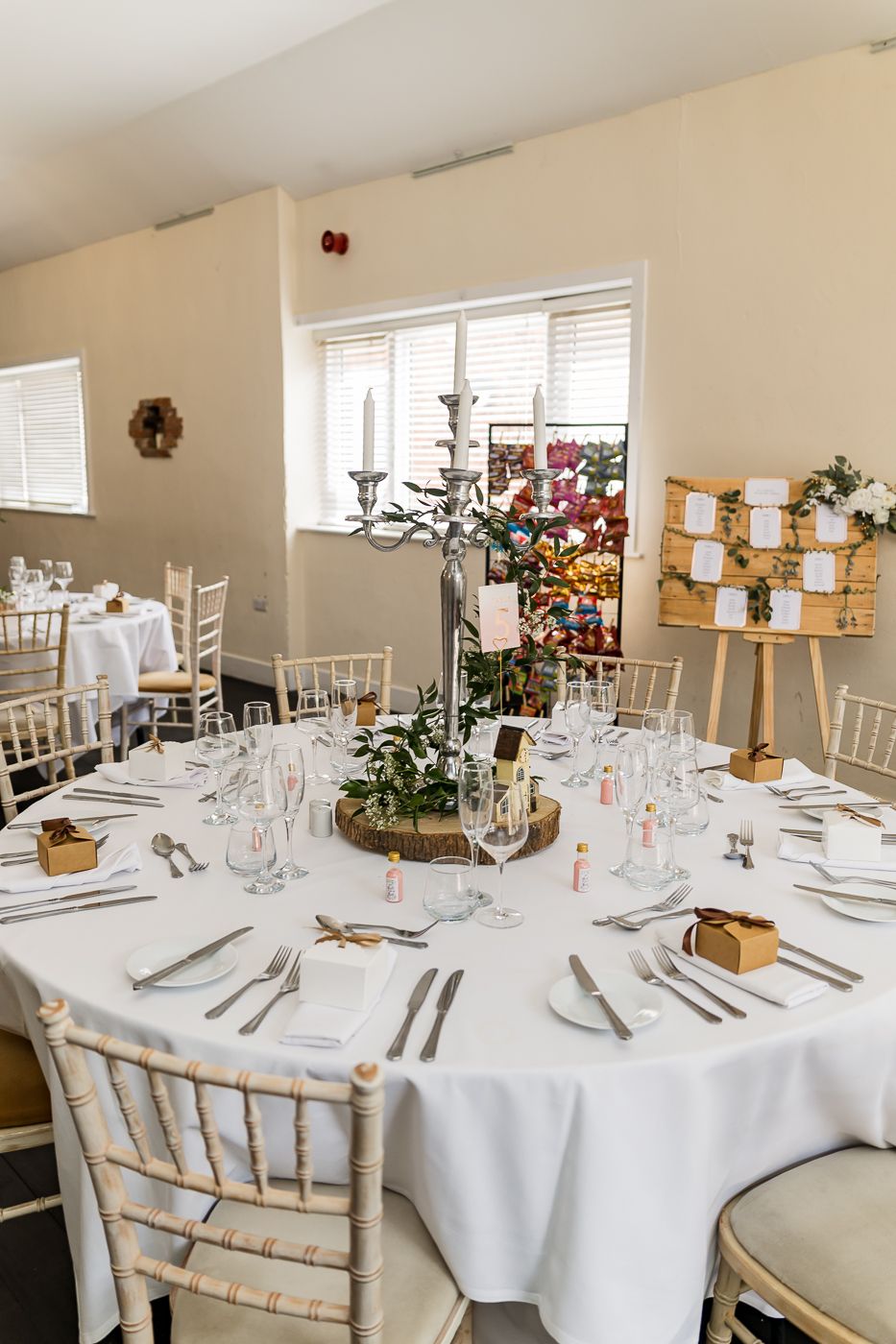 Elegant wedding reception table set with white linen, candelabra centerpiece, and Chiavari chairs in a bright venue.