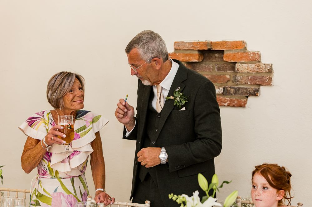 Elegant couple sharing a toast at a wedding reception, man in dark suit with boutonniere, woman in floral dress.