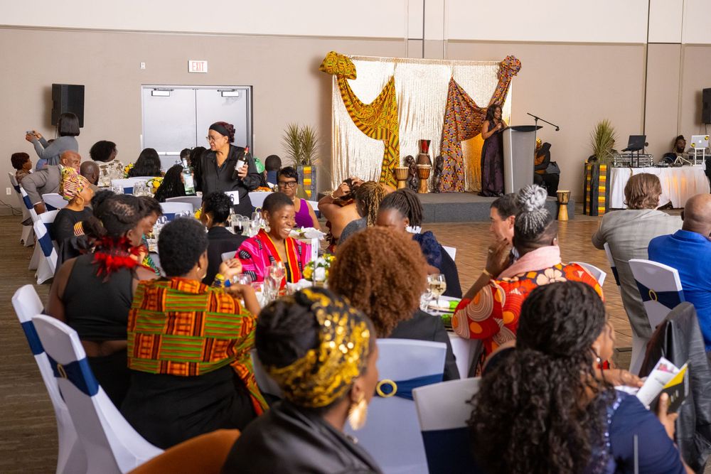 Guests in colorful African attire gather at a festive banquet hall event with decorative stage backdrop.