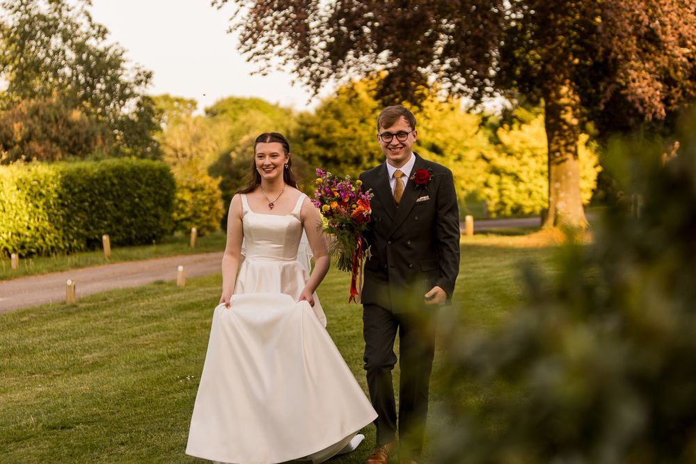Happy bride and groom walking outdoors in golden sunlight, bride in white gown holding colorful bouquet.