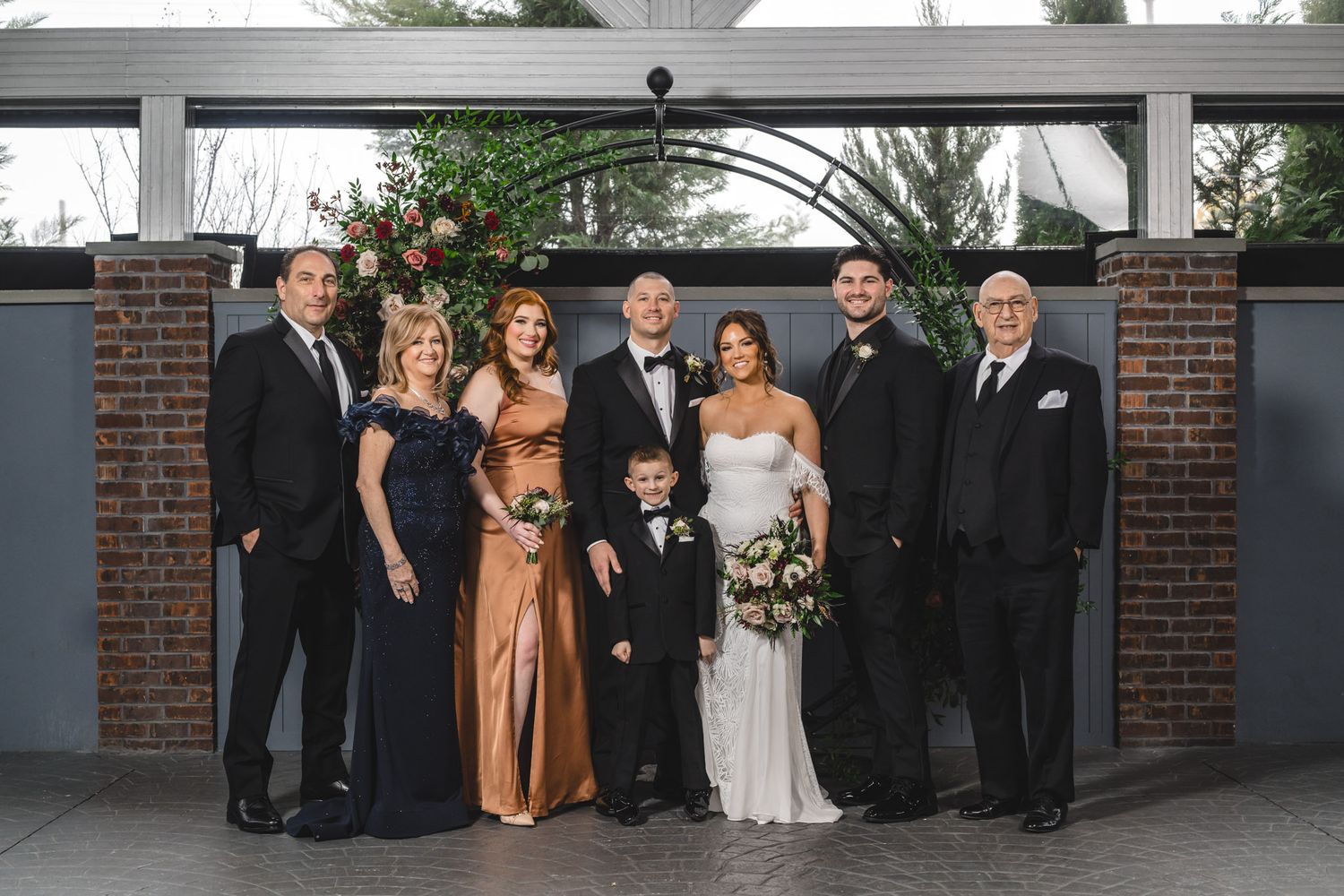 Wedding party poses together in formal attire outside a brick building.